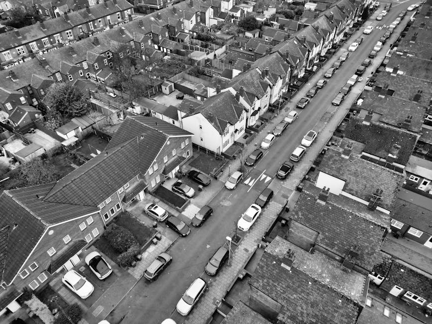 A row of terraced houses on a residential street in Catford, featuring brick facades, white window frames, and small front gardens enclosed by low brick and metal fences. The street is lined with park